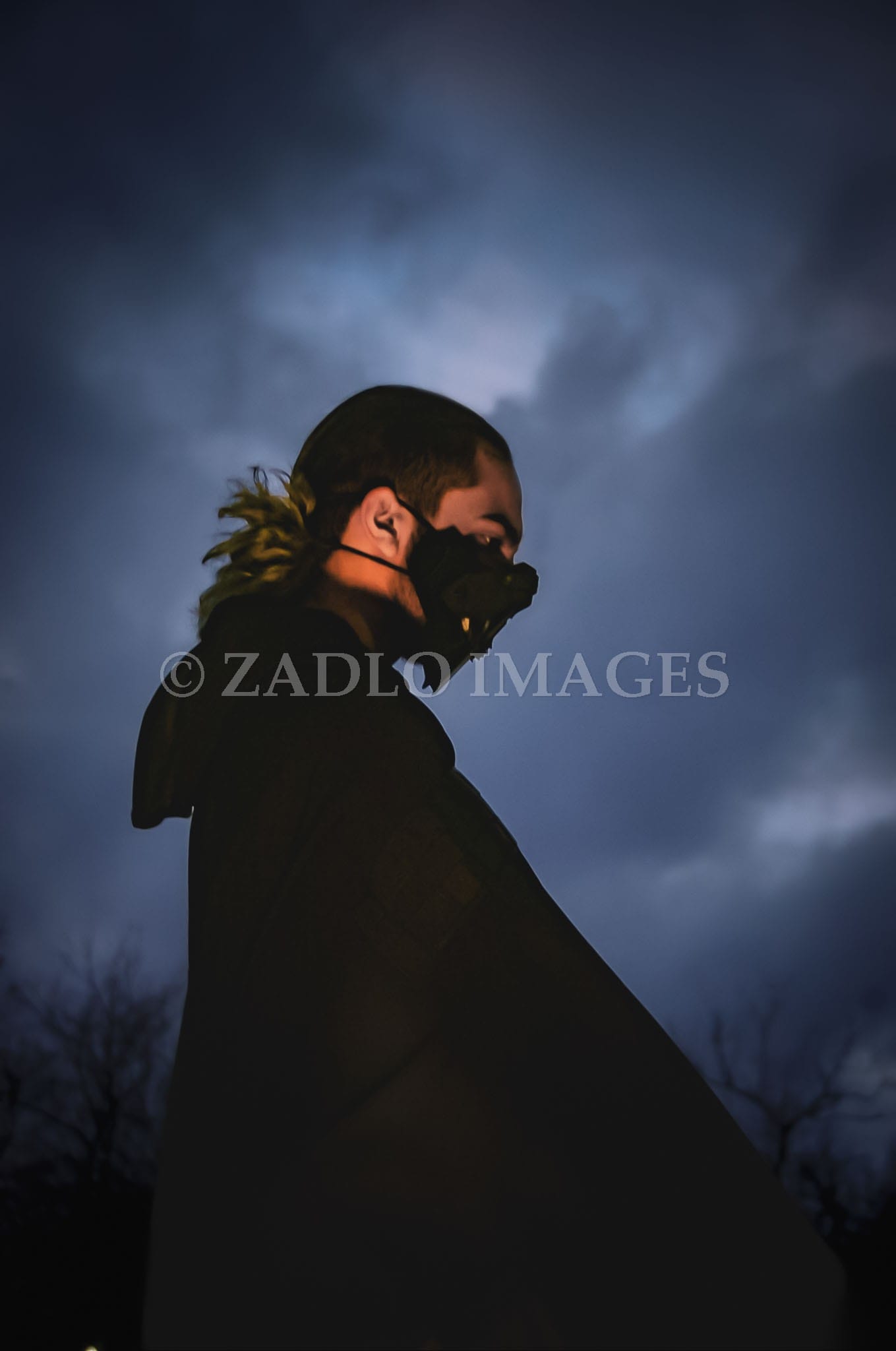 Teen boy wearing a cape with a dark gray sky in the background.