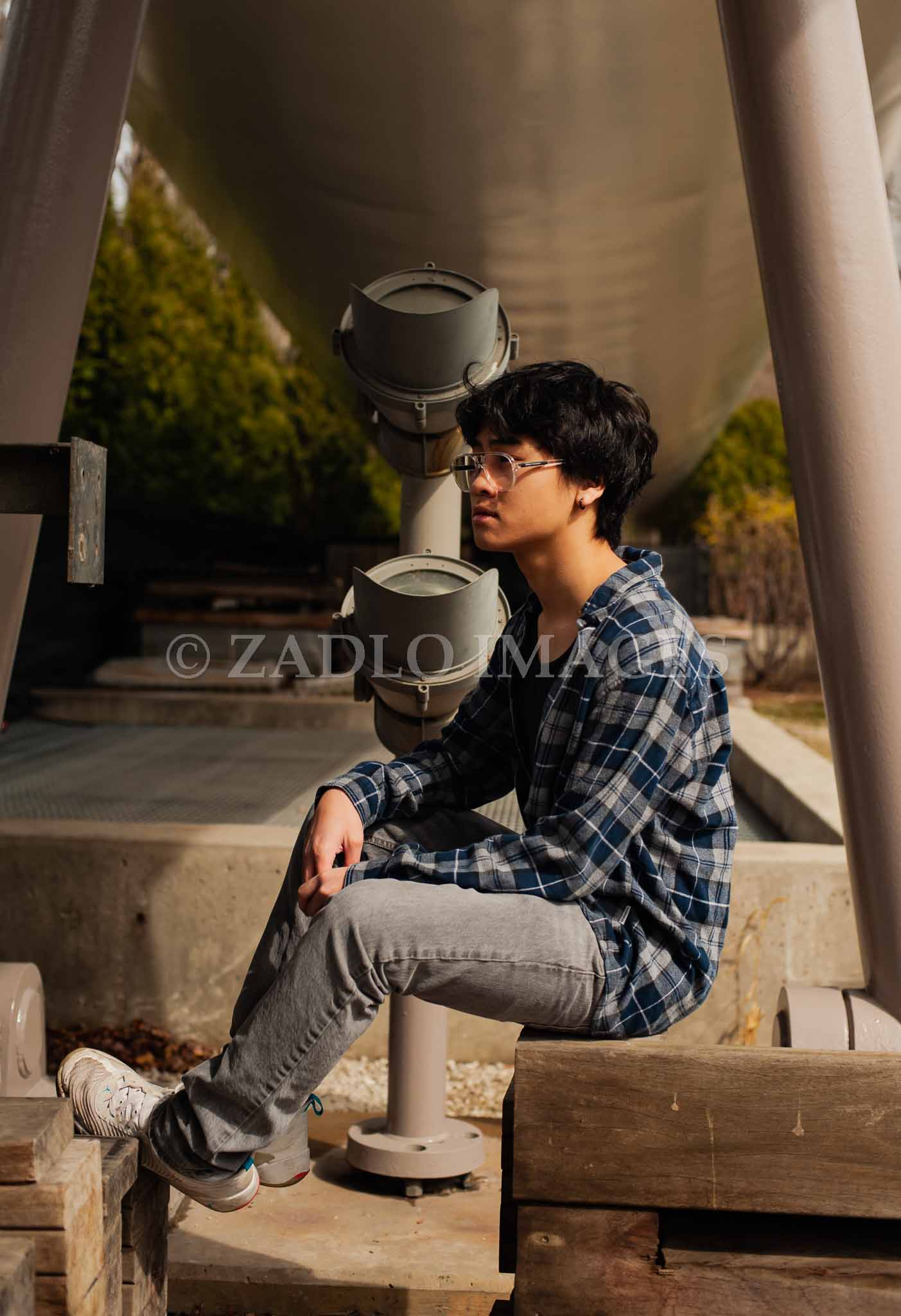 Teen boy sitting on crate under a bridge.